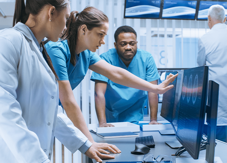 Three doctors are gathered around a screen, engaged in a discussion.