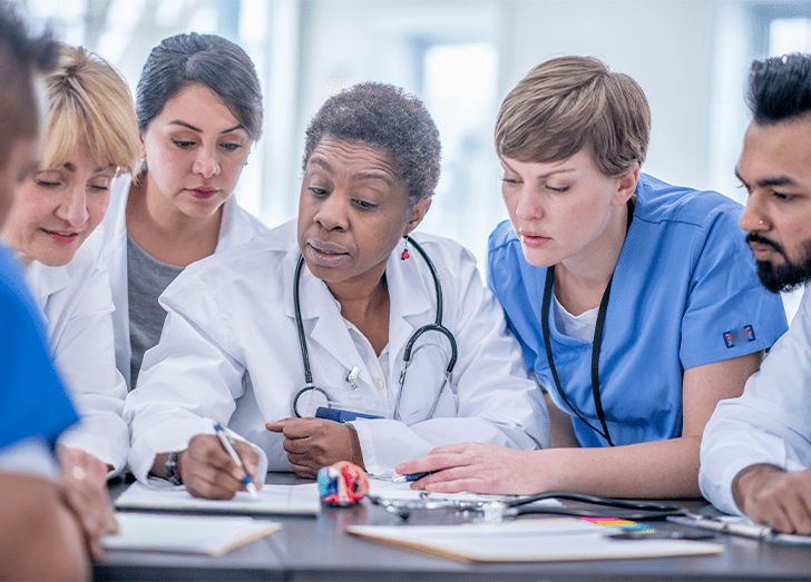 A woman doctor works with other doctors and nurses, explaining the course material to them.