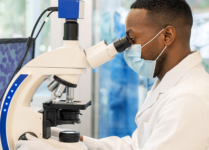 Man in mask looking at a microscope.