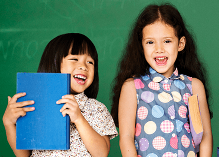 Children standing together smiling and holding books.