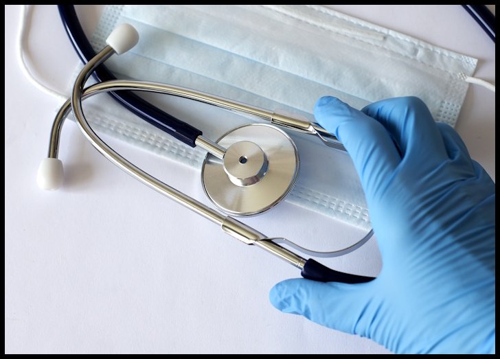 blue-gloved hand reaching for stethoscope on table on top of medical mask