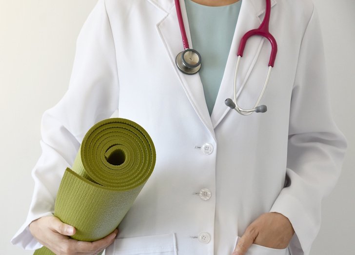 Physician torso in white coat with red stethoscope holding green yoga mat