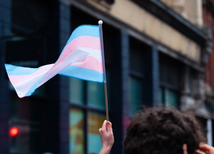 man holding transgender flag over head.