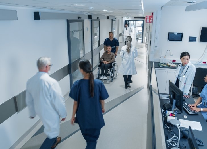 High Angle CCTV Shot with a Busy Hallway with Reception Desk of a Hospital Building, Diverse Female and Male Staff Members Walking, Working. Professional Nurses, Doctors and Personnel at Work