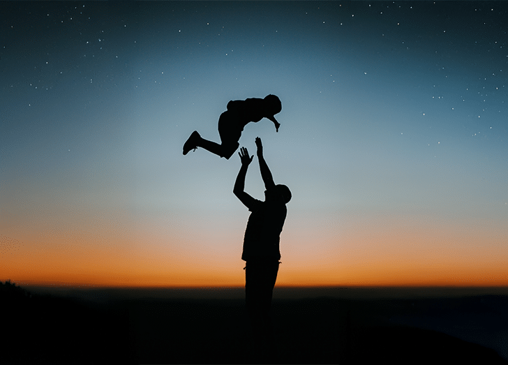 silhouette image of a male tossing his son in the air.