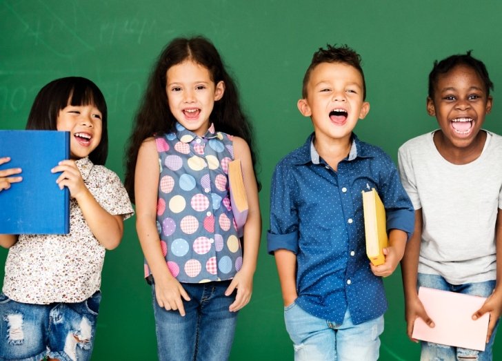 Children standing together smiling and holding books. 