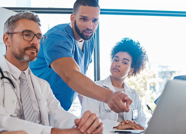 image of doctors sitting at a table looking at a laptop.