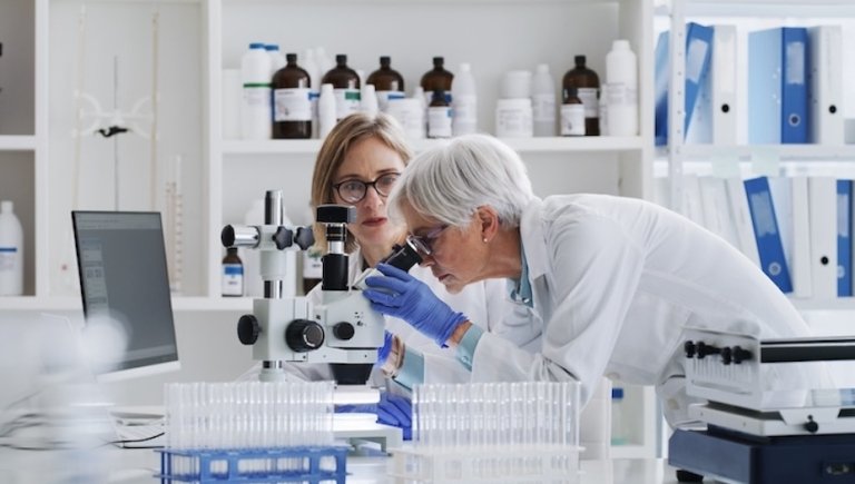 Two female scientists look through a microscope in a lab. 