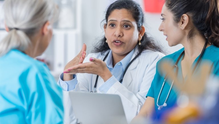 A female health care provider speaks to nurses in scrubs.