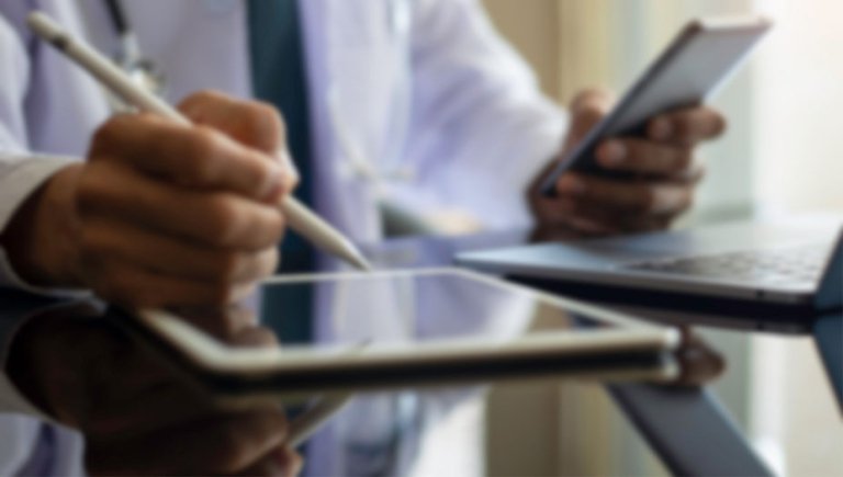 A zoomed in photo of a person writing on a tablet and holding a mobile phone.