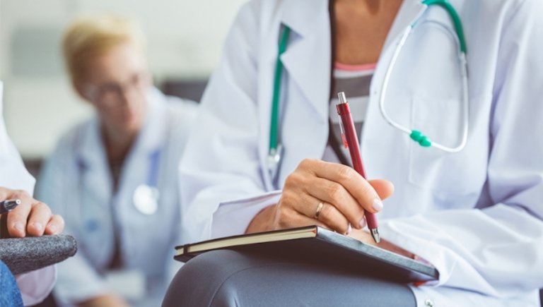 Doctor takes notes surrounded by colleagues. 
