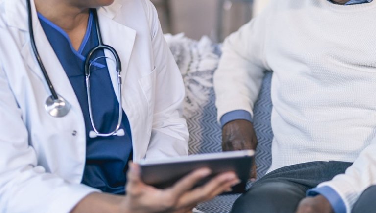 A zoomed photo of a doctor speaking with a patient, holding an ipad.