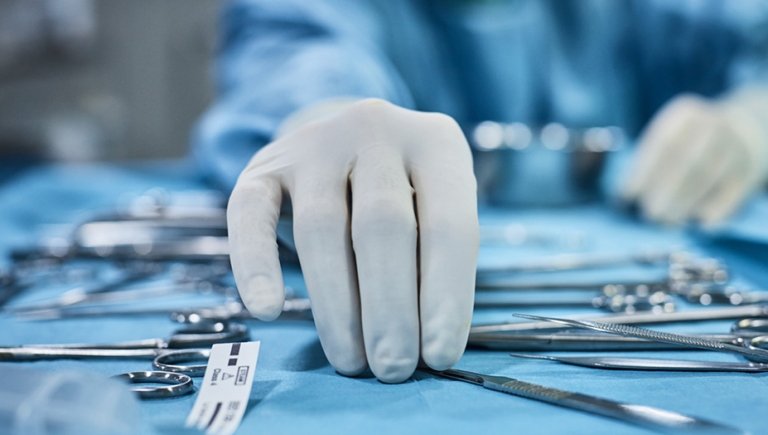 Physician's hand with rubber glove holding medical instrument. 