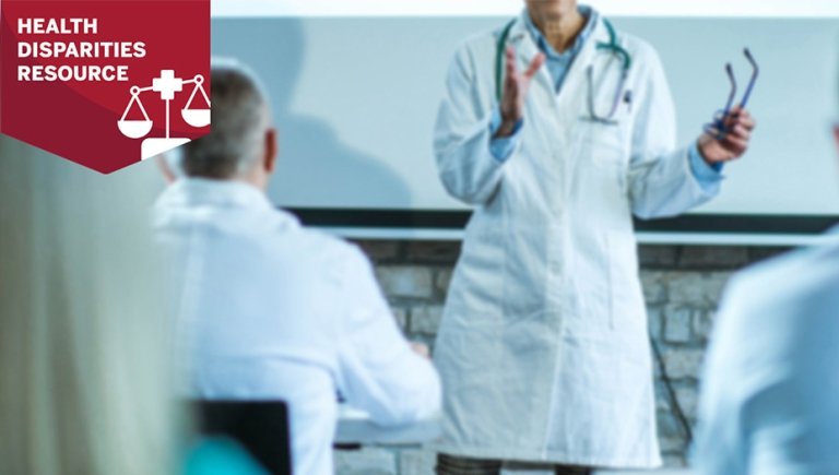 Physician at the front of a classroom teaching a group of medical students.