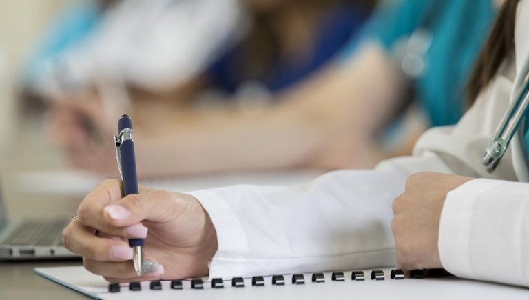 Woman's hand holding a pen to a piece of paper during a lecture.