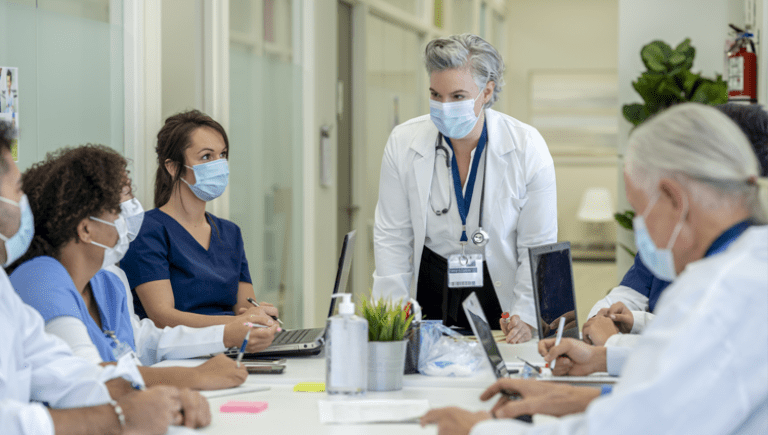 female doctor standing and talking to a group of doctors at a table.