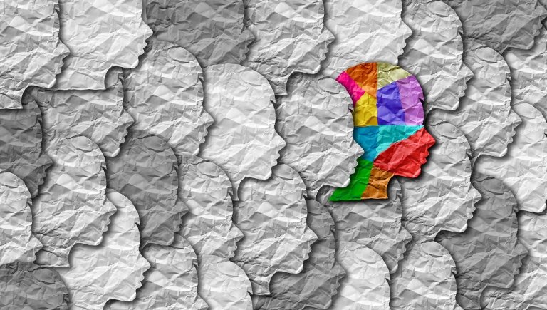 collage of paper outlines of heads in grey, and one colorful one.