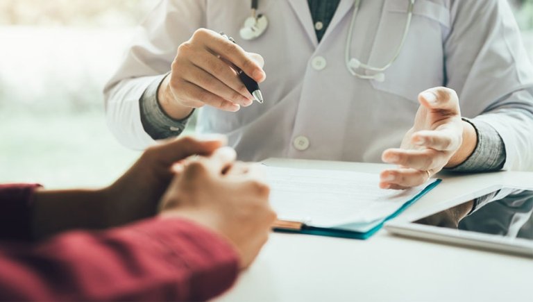 A zoomed in photo of a doctor with a pen talking to a patient writing notes.