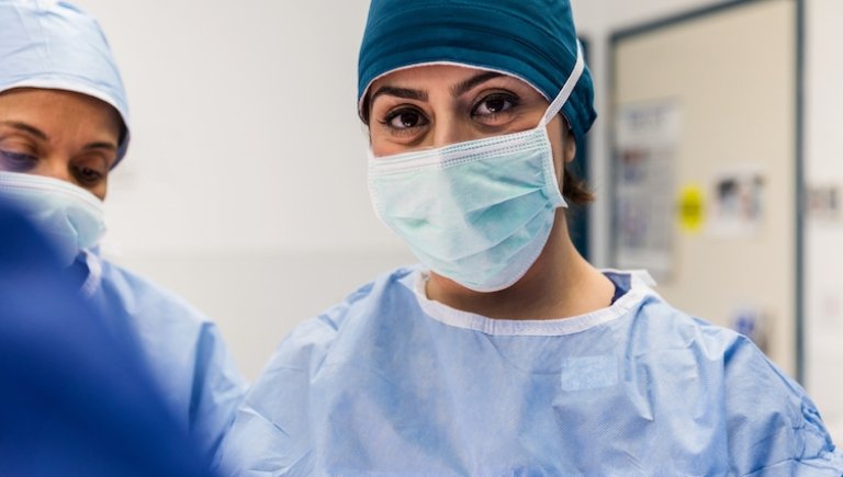 female surgeon with mask on smiling into camera.
