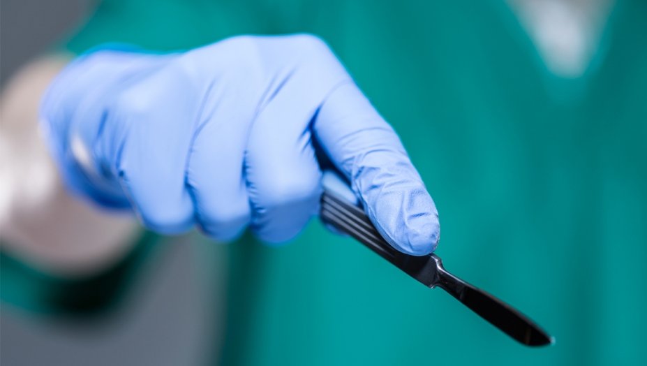 A close up image of a gloved hand holding a scalpel.