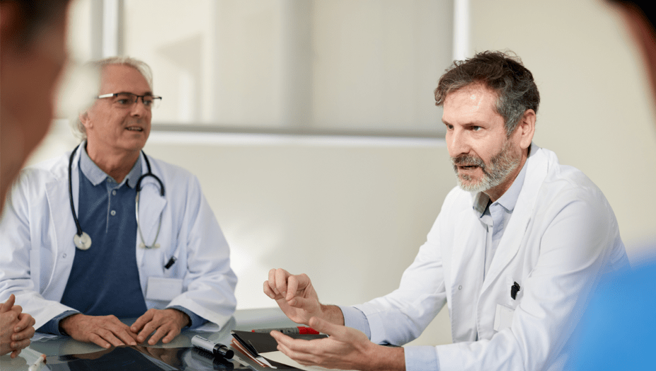male doctors sitting at a table having a conversation.