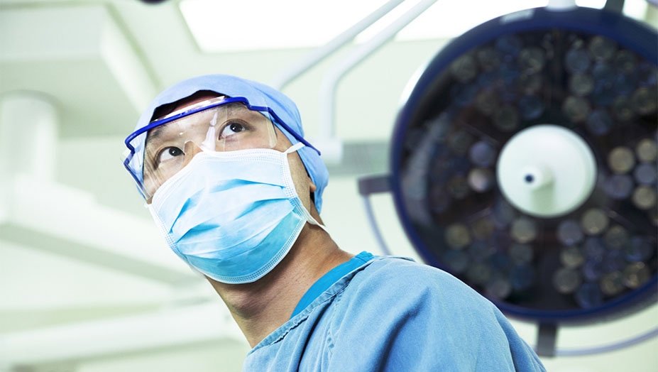 A photo of a health care professional with a blue mask and eye goggles looking up.