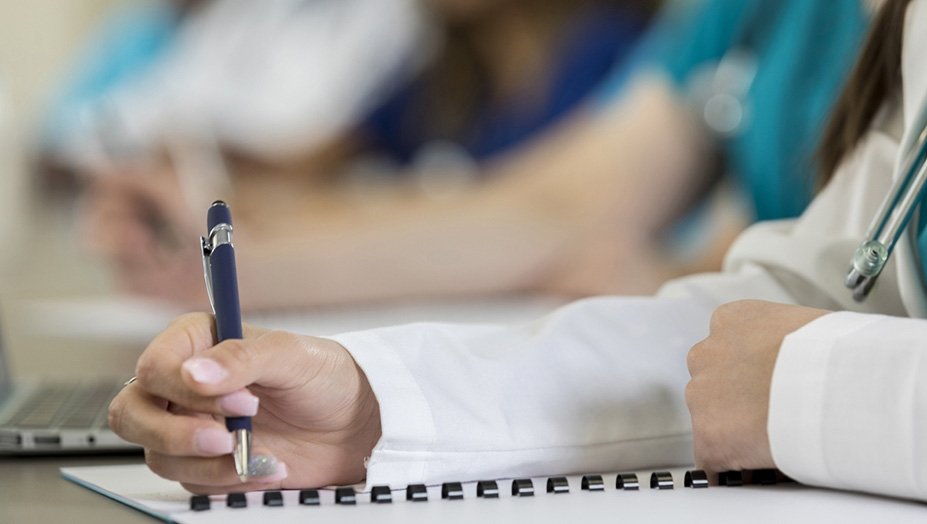 Woman's hand holding a pen to a piece of paper during a lecture.