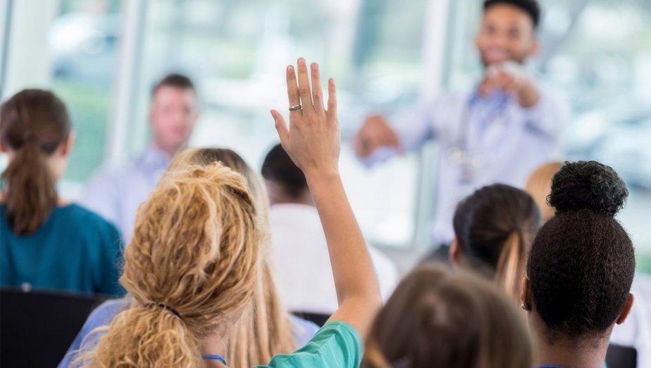 female participant raising her hand during a lecture, waiting to be called on.